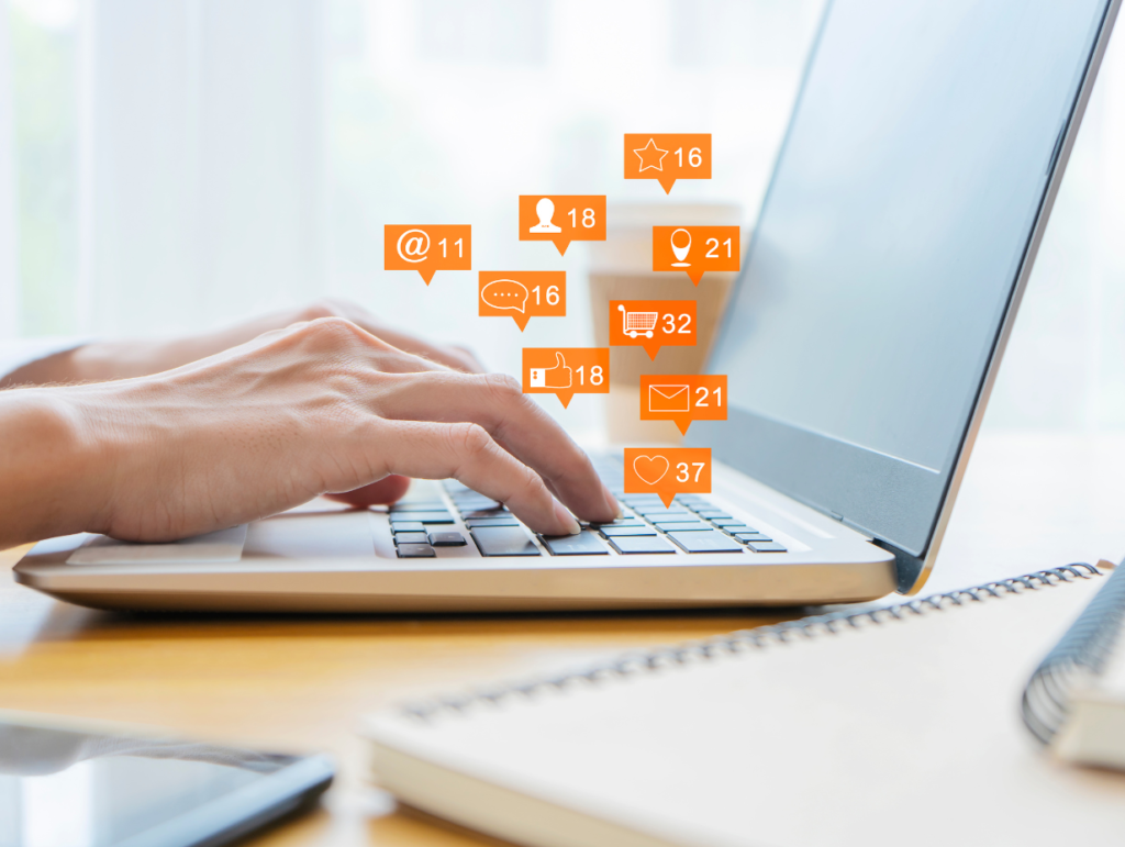 Gros plan sur des mains tapant sur un clavier d’ordinateur portable, entourées d’icônes numériques représentant des notifications, des interactions et des messages sur les réseaux sociaux.